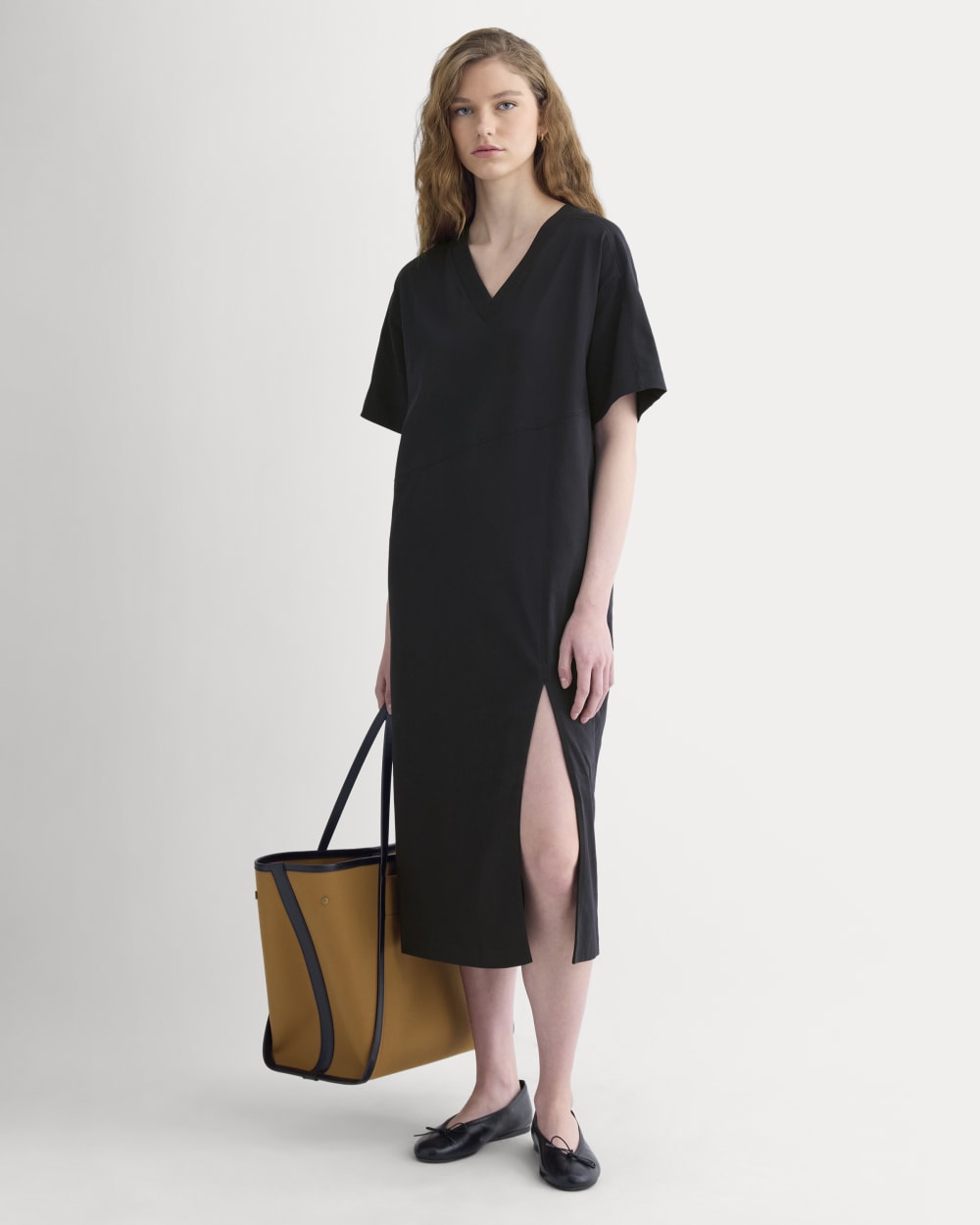 Oversized black V-neck T-shirt midi dress with elbow-length sleeves and a front slit, styled with a tan and black tote